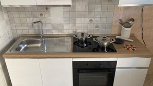Une cuisine équipée d’un évier, d’une cuisinière, d’un four et d’un plan de travail recouvert de carreaux blancs.