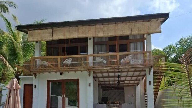 Un edificio de dos pisos con un balcón, una zona de estar al aire libre techada y una piscina.