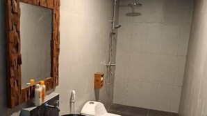 Un baño con espejo de marco de madera, lavabo negro, inodoro blanco y ducha.