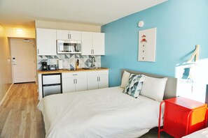 Habitació d'hotel amb un llit, una cuineta petita i una paret blava.