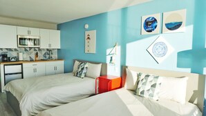 Ein Hotelzimmer mit zwei Betten, einer Küchenzeile und einer blauen Wand mit Kunstwerken.