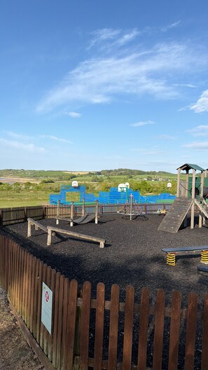 Ein Spielplatz mit Holzzaun, Schaukeln und einer Rutsche.