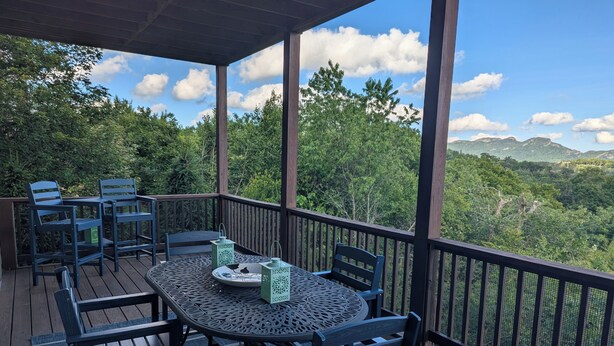 A covered outdoor deck with a table and chairs, surrounded by a mesh railing, overlooking a forested landscape. - Walk to the slopes!  2BR in The Reserve with iconic Grandfather Mountain views (Sugar Mountain)