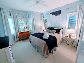 A bedroom with a bed, bedside tables, a dresser, a ceiling fan, and a window with curtains.
