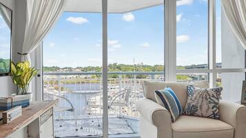 A balcony with a view of a river and buildings, a sofa with patterned cushions, and a plant on a table.