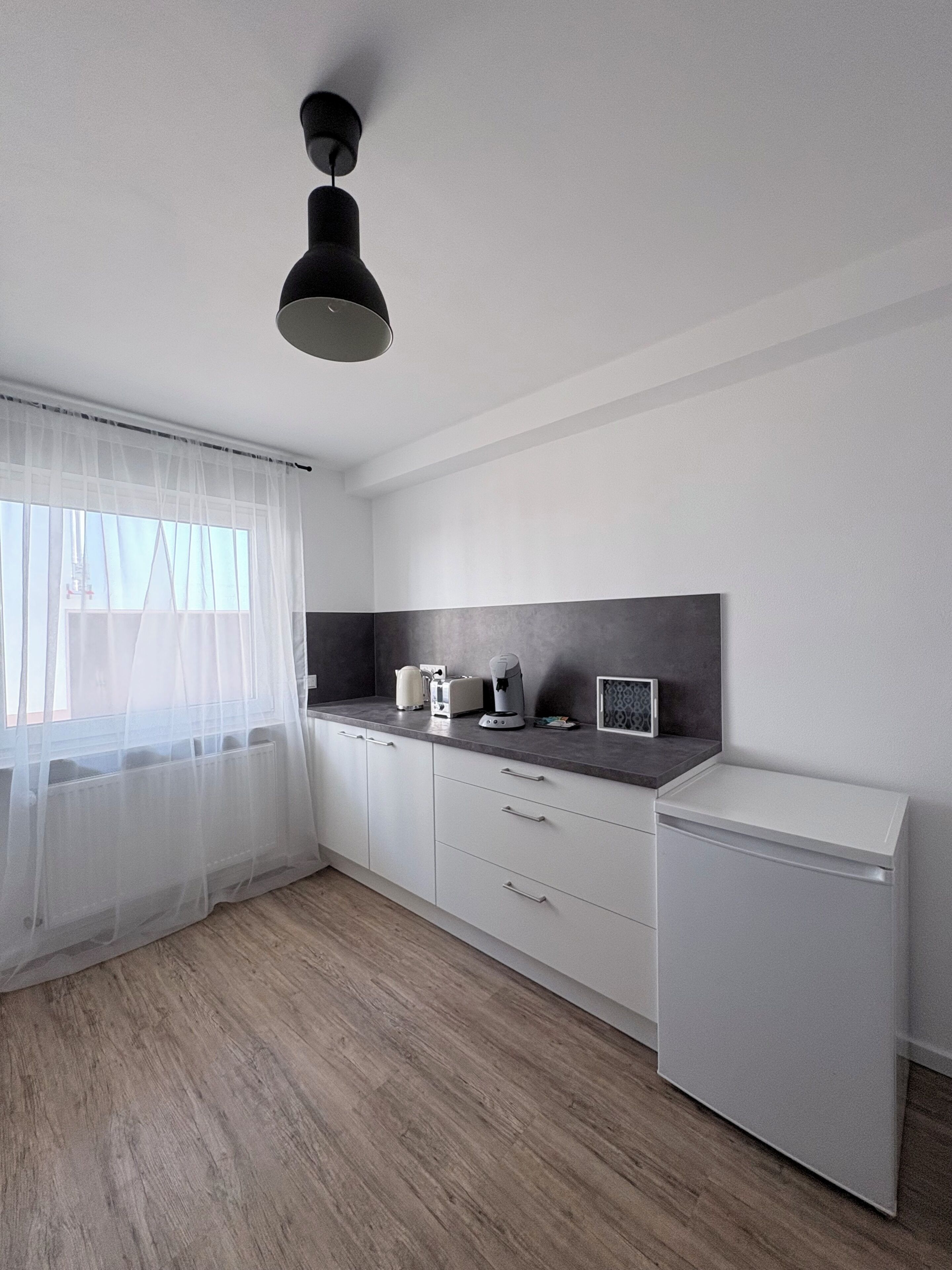 A modern kitchen with white cabinetry, a built-in microwave, and a small refrigerator.