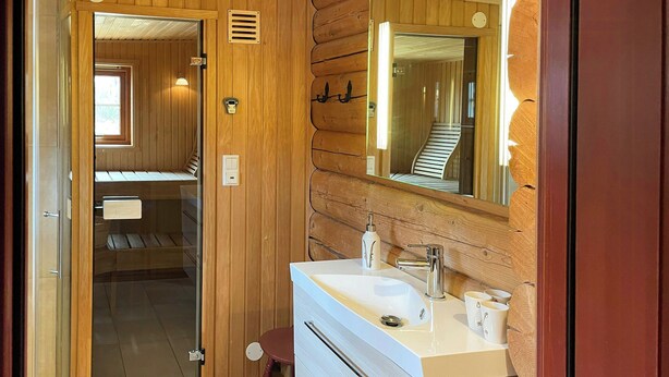 A wooden interior with a bathroom featuring a sink, mirror, and towel rack.