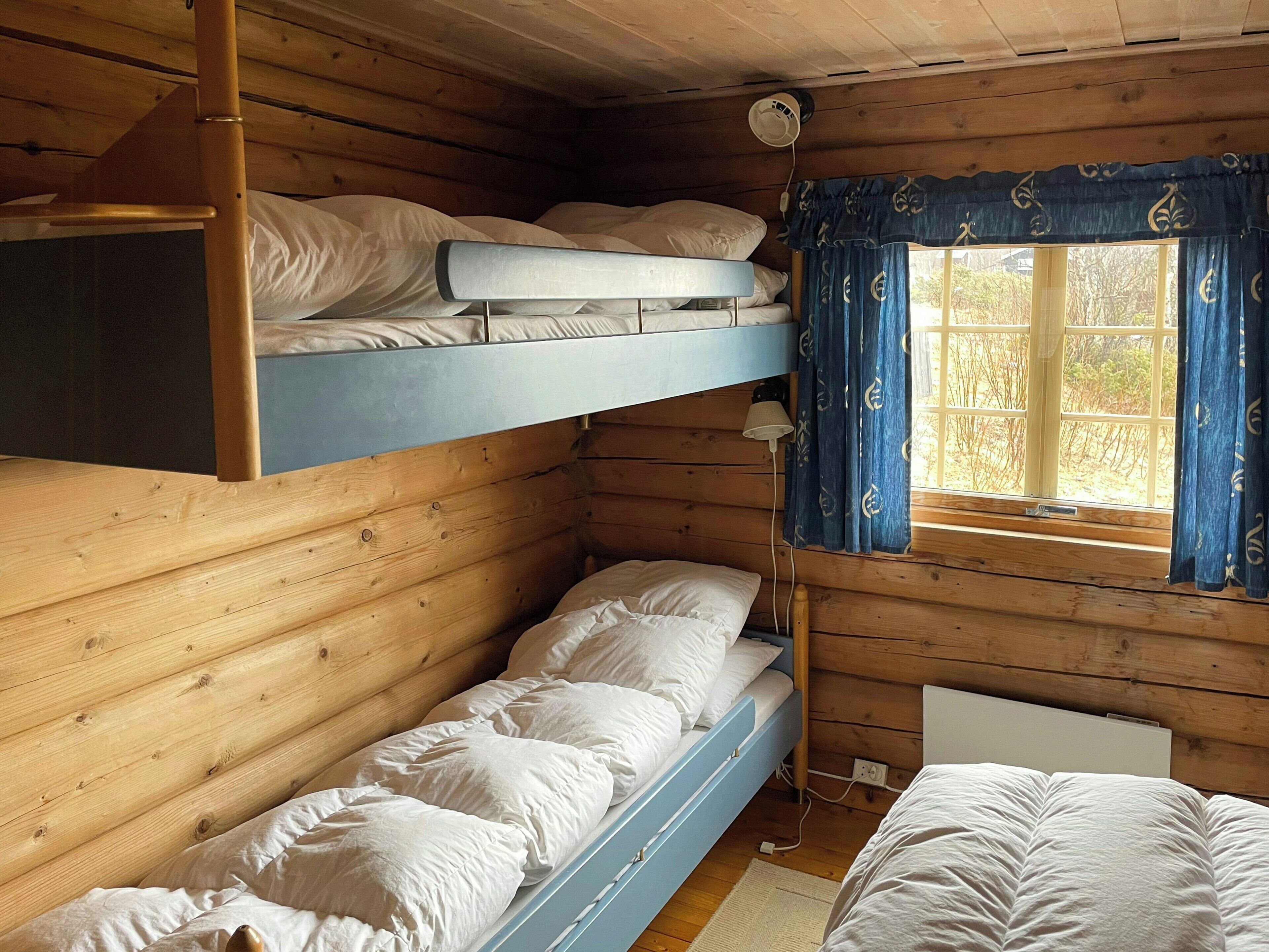 Habitación con literas, paredes de madera, una ventana con cortinas y una lámpara de noche.