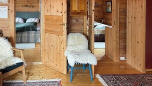 A wooden cabin interior with a bed, a chair, a small table, and a cabinet.
