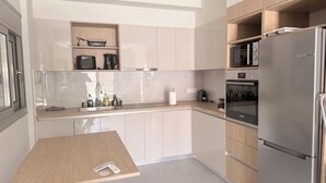 Een moderne keuken met een houten tafel, roestvrijstalen apparatuur en lichtkleurige kastjes.