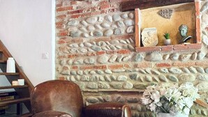 Una pared de piedra con una estantería, un sillón de cuero y una planta en maceta.