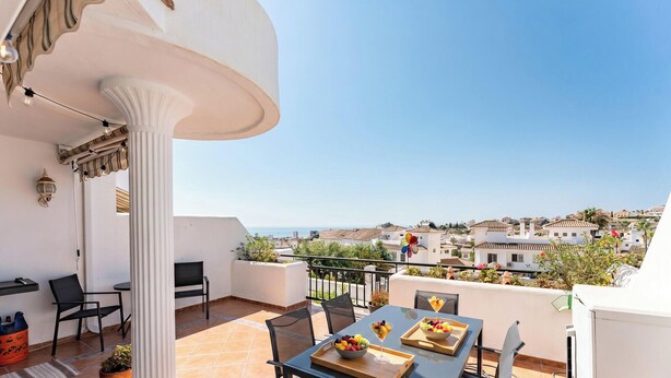 Ein Balkon mit Tisch und Stühlen für zwei Personen, einem Blumentopf und Blick auf eine Küstenstadt.