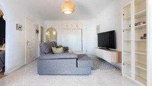 Ein Wohnzimmer mit grauem Sofa, einem Fernseher und einem Bücherregal.