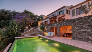 Area piscina con muro in pietra, una scala che conduce a un edificio e sedie a sdraio.