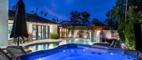 Ein Swimmingpool mit Whirlpool, Sitzgelegenheiten im Freien und ein Haus mit großen Fenstern und einer überdachten Terrasse.