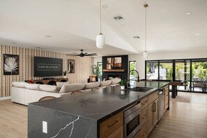 A modern kitchen with a large island, a dining area, and a living space with a sofa and a fireplace. - Solterra - Heated Pool, Hot Tub, Sauna, Pickleball (Scottsdale)
