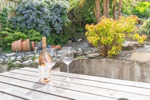 A wooden table with a bottle and two glasses, surrounded by greenery and plants. - Highfield Terrace - Imposing, Beautiful Victorian House With Stunning Sea Views (Ilfracombe)