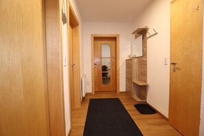Un couloir étroit avec des portes en bois, un paillasson noir et un miroir au mur.