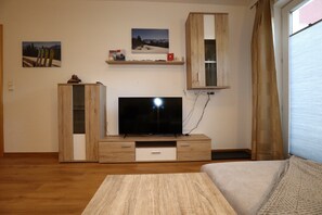 A living room with a flat-screen TV, wooden cabinets, a sofa, and a window with curtains. - Apartment in Strengen With Mountain Views (Strengen)
