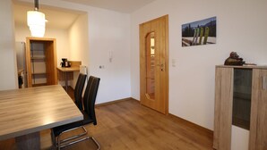 A dining area with a wooden table and chairs, a kitchen area with a refrigerator and cabinets, and a wooden door leading to another room. - Apartment in Strengen With Mountain Views (Strengen)