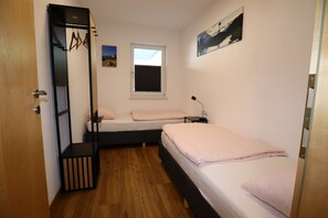 Une chambre avec deux lits, une fenêtre, une porte et une petite table avec une lampe.