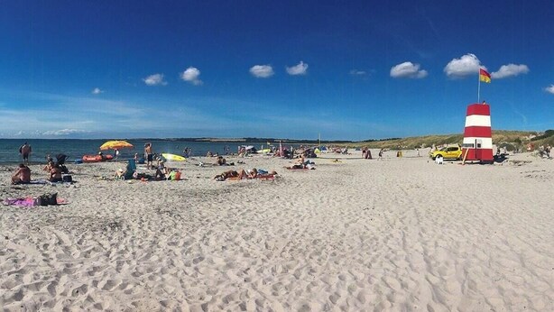 A beach with people sunbathing, umbrellas, and a lighthouse. - Secluded holiday oasis near lovely beach (Højby)