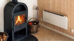 A room with a black wood-burning stove, a white radiator, and a wooden wall with a framed picture. - Secluded holiday oasis near lovely beach (Højby)
