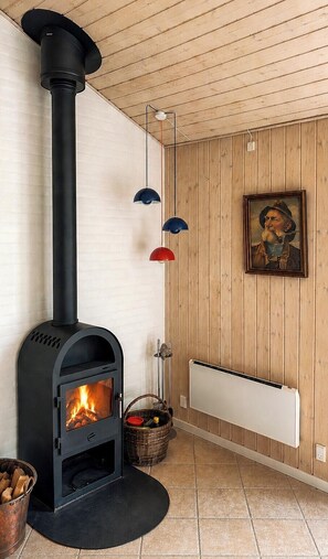Une pièce avec un poêle à bois noir, un radiateur blanc et un mur en bois orné d’un tableau encadré.