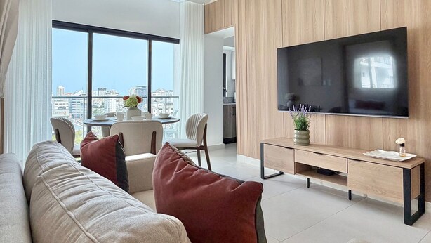 A modern living room with a sofa, a dining table, and a TV mounted on a wooden wall. - City Center| Pool and Gym 1BR by YellowKey (Santo Domingo)