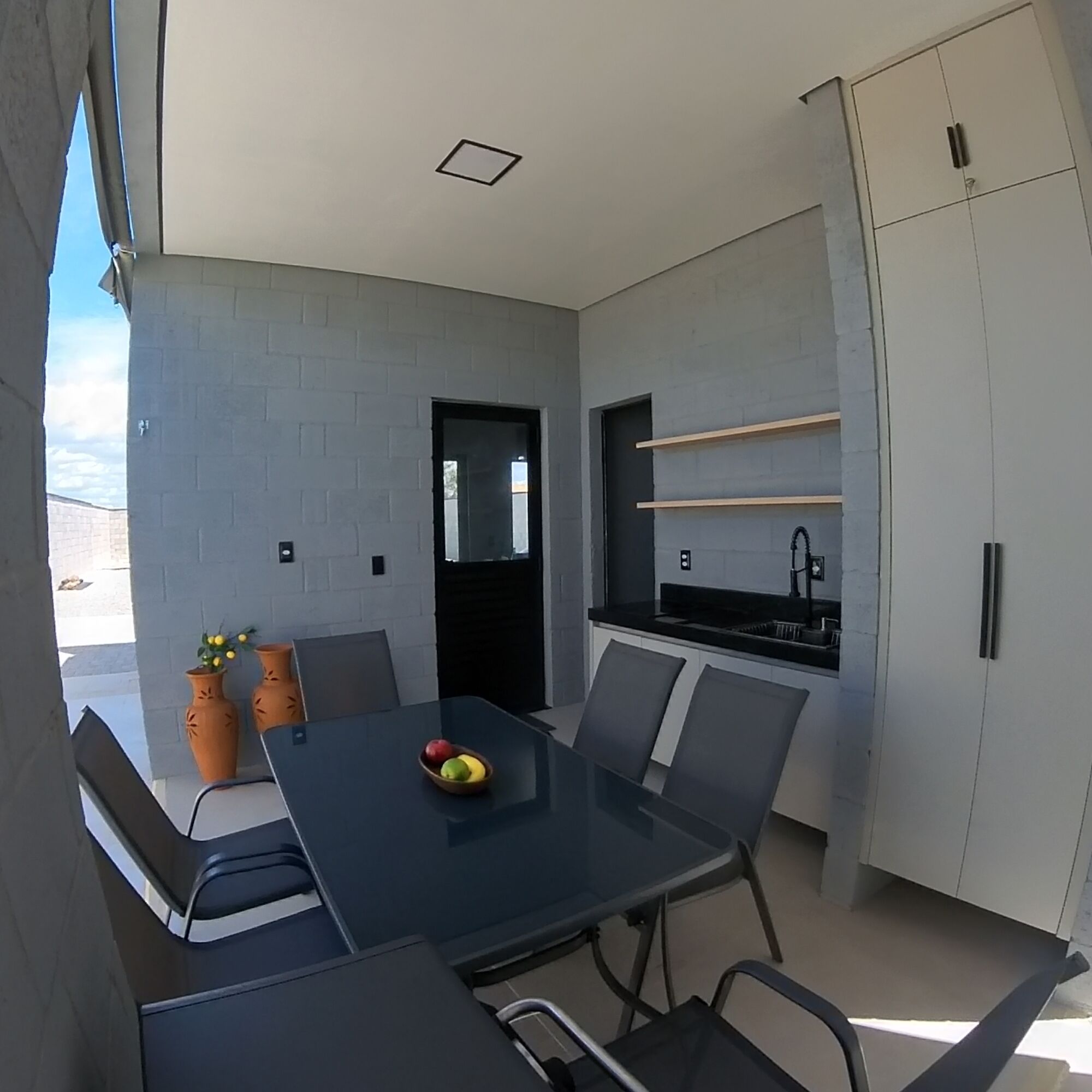 A modern kitchen with a dining area, featuring a black table, grey chairs, and a small fruit bowl.