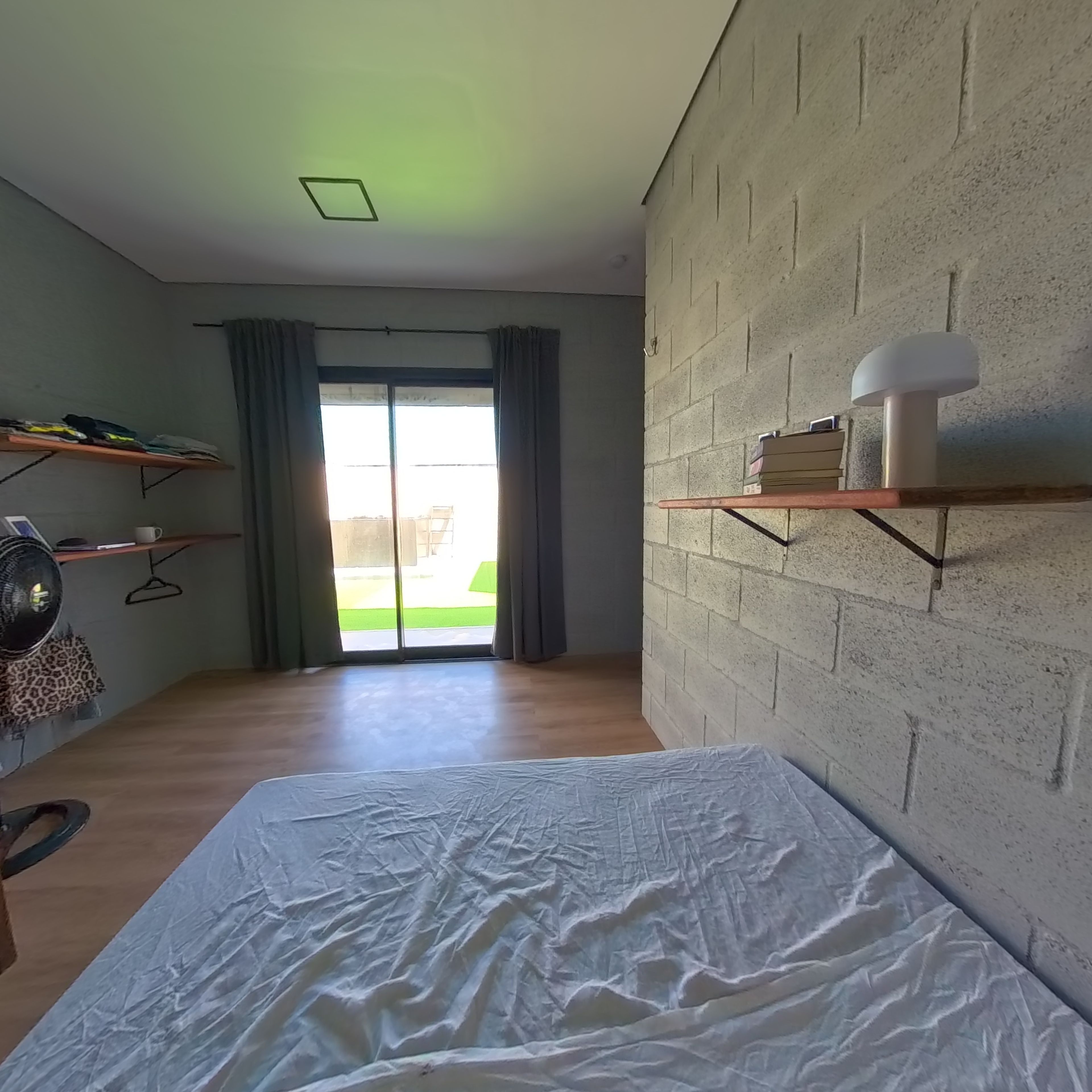 Une chambre à coucher avec un lit, une armoire, une étagère remplie de livres et une vue sur l’extérieur, visible à travers une porte coulissante.