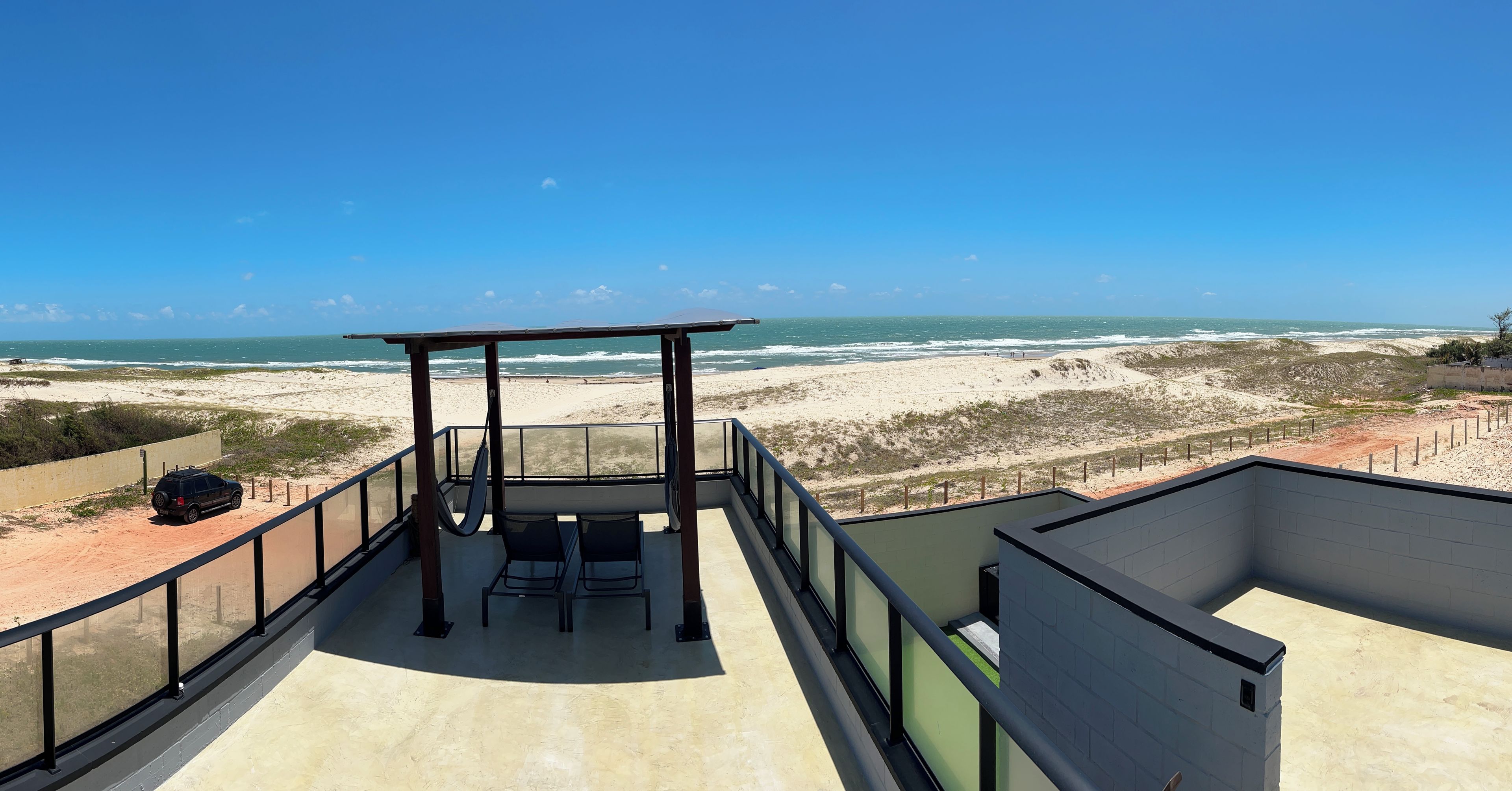 A balcony with a view of the beach, a table, and chairs.