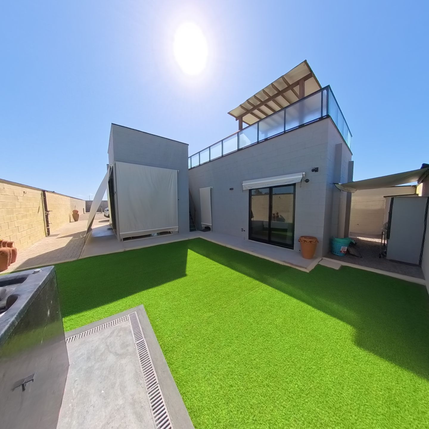 A modern building with a flat roof, a covered patio area, and a green artificial lawn.