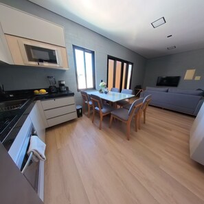 A modern kitchen with a microwave, stove, and sink. There is a dining area with a table and chairs. A gray sofa is in the living area. - Ocean Paradise Villa Aguas Belas (Caponga)
