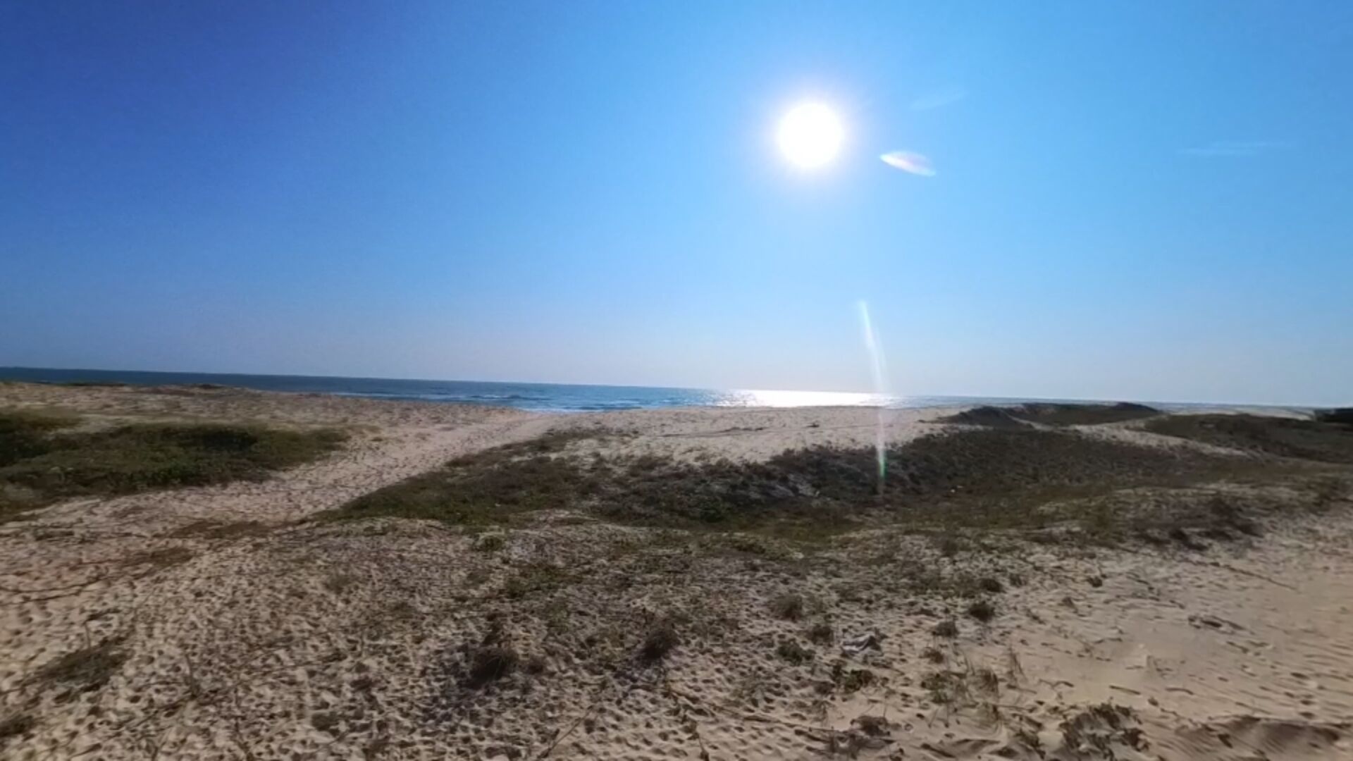 Une plage avec un ciel dégagé et un sentier sablonneux menant à l’eau.