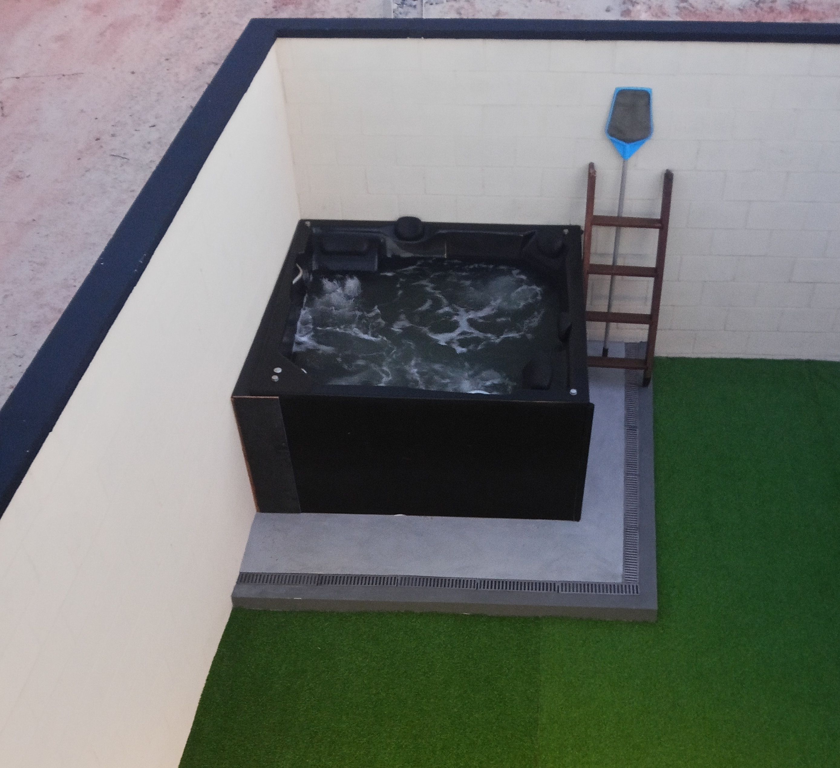 Un jacuzzi en un rincón de la habitación, con una escalera y césped artificial.