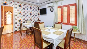 Un coin repas avec un mur décoré de motifs, un ventilateur de plafond, un téléviseur et une fenêtre avec des rideaux.