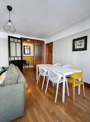 A dining area with a white table and chairs, a grey sofa, and a wooden floor. - Charming Apartment in the Heart of Épinal (Épinal)