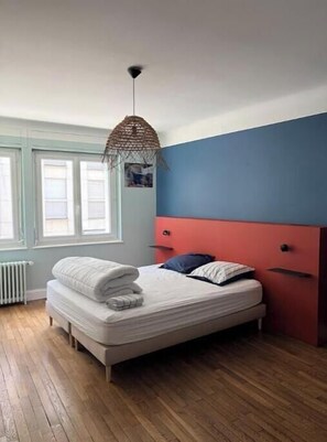 A bedroom with a bed, a window, a radiator, and a hanging light fixture. - Charming Apartment in the Heart of Épinal (Épinal)