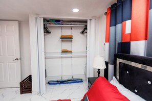 Ein Schlafzimmer mit einem Bett, einem Nachttisch, einer Lampe, einem Kleiderschrank mit Regalen und einer Tür.