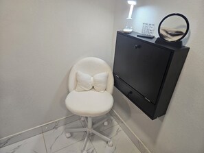 Ein weißer gepolsterter Sessel mit Fußstütze, eine schwarze Kommode mit Spiegel und eine Wandlampe.