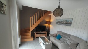Un salon avec un escalier, un canapé, une table basse et un luminaire suspendu.