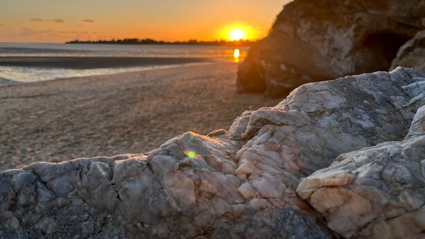 Une scène de plage avec un coucher de soleil, des formations rocheuses et un ciel dégagé.