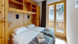 Ett rum med två sängar, träpanel på väggarna, en balkong med ett träräcke och ett fönster med utsikt över ett snötäckt landskap.
