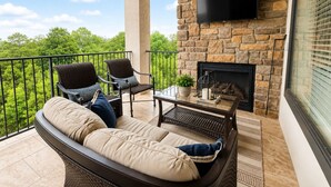 Un balcon aménagé avec un canapé, des chaises, une table, une cheminée et un téléviseur.
