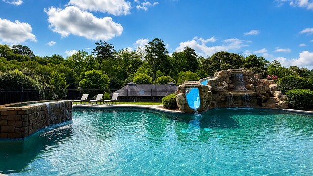 Une piscine d’un bleu éclatant, agrémentée d’une cascade, entourée d’une terrasse en pierre et de chaises longues.
