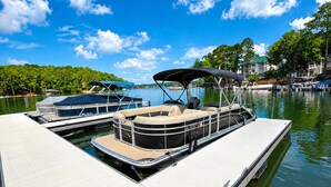 Un bateau amarré avec un espace de repos couvert, un plus petit bateau doté d’un auvent bleu, et un bâtiment avec un toit vert en arrière-plan.