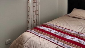 Une chambre à coucher avec un lit, une fenêtre avec un rideau et un luminaire fixé au mur.