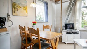 A cozy room with a wooden dining table, chairs, a painting, a coffee maker, a TV, and a ladder. - Pet-friendly Home in Callanstoog Near Beach (Callantsoog)