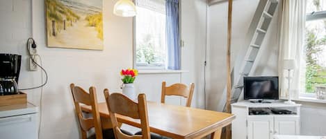 A cozy room with a wooden dining table, chairs, a painting, a coffee maker, a TV, and a ladder.